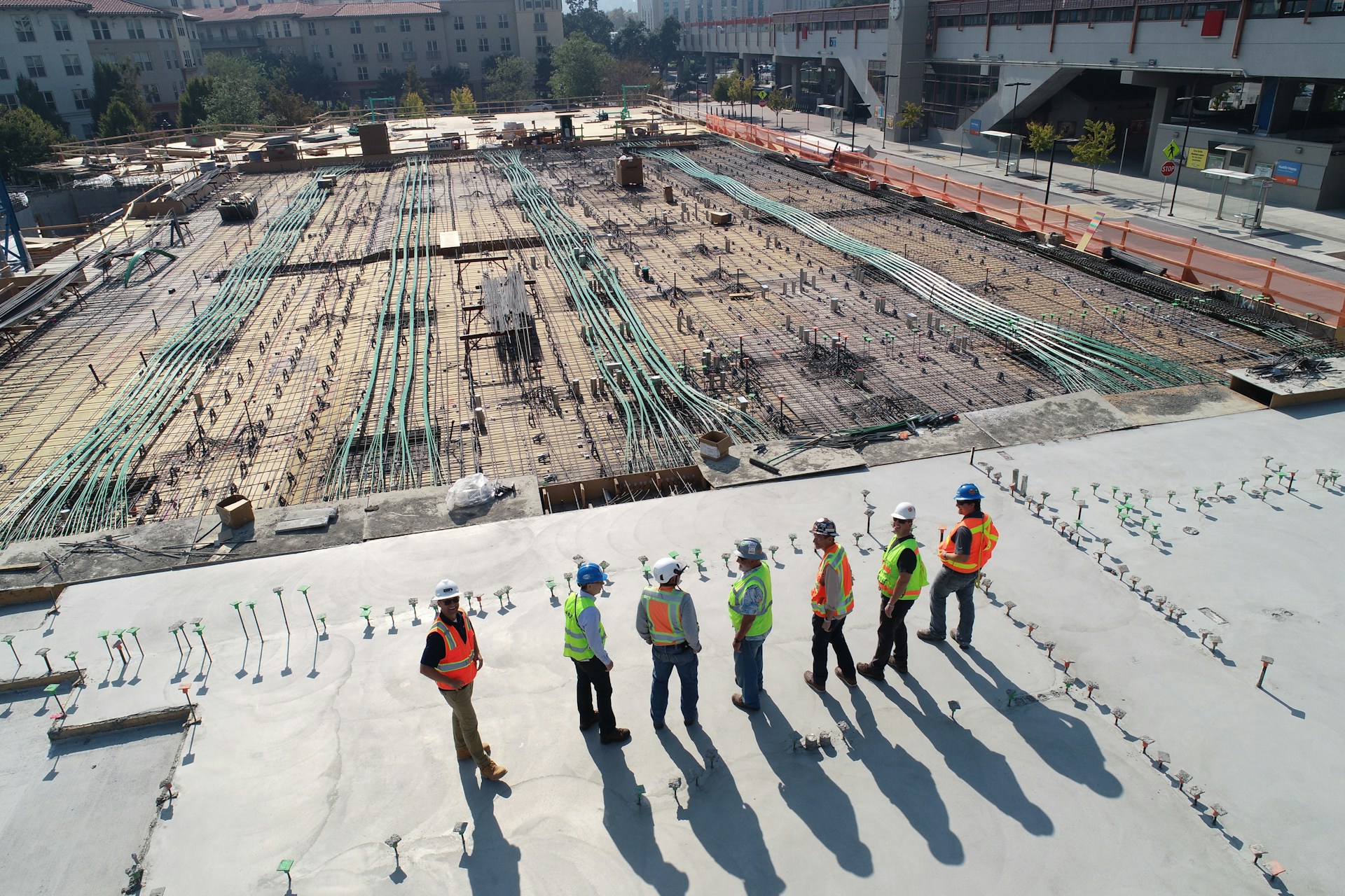 Construction workers in hard hats and safety vests overlooking a steel rebar grid on a commercial construction jobsite
